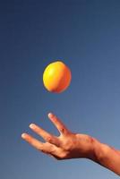 mano femenina equilibrando naranja en el aire foto