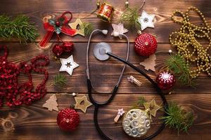 Christmas flat lay on a medical theme. Decorations for the new year from stars, ball, ribbons, Santa hats, and a doctor's stethoscope. Wooden background, space for text photo