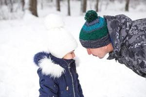 Dad and daughter look at each other closely in warm clothes, hats with a pompom on the street in winter. Family outing, active entertainment, parenting. photo