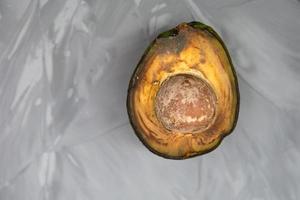 Spoiled avocado with green mold and black spots of rot and fungus on a gray background. Cut natural fruit, half with a round bone. Space for text photo