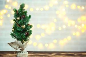 A small Christmas tree stands on a table with fairy lights in bokeh. Copy space and empty space photo