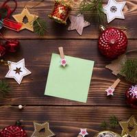 Christmas flat lay of red balloons and wooden stars and clothespins on a dark background with a square sheet for notes in the center. New year's frame, space for text. Xmas toys, beads, pine branches photo