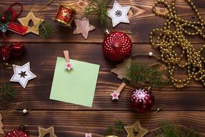 Christmas flat lay of red balloons and wooden stars and clothespins on a dark background with a square sheet for notes in the center. New year's frame, space for text. Xmas toys, beads, pine branches photo