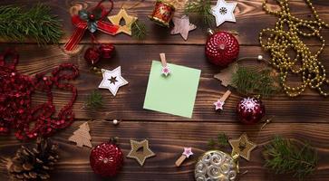 Christmas flat lay of red balloons and wooden stars and clothespins on a dark background with a square sheet for notes in the center. New year's frame, space for text. Xmas toys, beads, pine branches photo