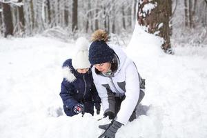 Mom and daughter play snow games, build a fortress, make snowballs. Winter entertainment outside, active recreation, fun in the cold in warm clothes. Outdoor recreation, fun childhood, strong family photo