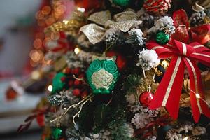 Christmas decor artificial Christmas tree close-up. Red and green toys, ribbons, glass owl, snow. Lights of garlands in the box. New year background photo