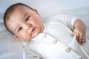 Cute portrait of a baby in a crib close-up. A child in white clothes on white underwear. Tenderness and care, children's problems. photo