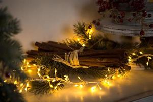 Cinnamon sticks tied with string in yellow lights garlands on Christmas tree branches and red berries. The atmosphere of the new year festive background, details of decorations photo