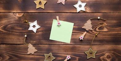 Christmas flat lay of wooden stars, fir trees and clothespins on a dark background with a square sheet for notes in the center. New year's frame, space for text. Xmas toys, to do list, a postcard photo