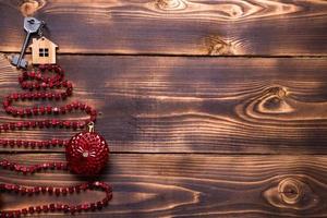 Key to the house with a keychain on top of Christmas tree made of red square beads. Flat lay on wooden background. Building or buying a house in new year. Mortgage, real estate rental. Space for text photo