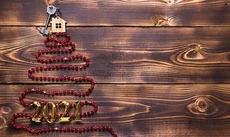 Key to the house with a keychain on top of Christmas tree made of red square beads. Flat lay on wooden background. Building or buying a house in new year. Mortgage, real estate rental. Space for text photo