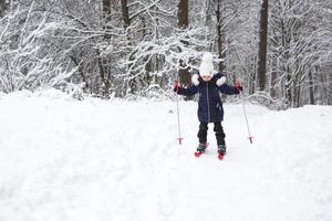 Children's feet in red plastic skis with sticks go through the snow from a slide-a winter sport, family entertainment in the open air. A little girl glides down the slope from an early age. Copy space photo