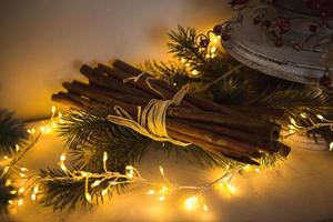Cinnamon sticks tied with string in yellow lights garlands on Christmas tree branches and red berries. The atmosphere of the new year festive background, details of decorations photo