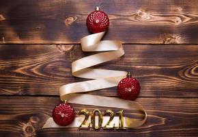 A Christmas tree made of gold ribbon with the numbers 2021 is decorated with red balloons on a dark wooden background. Flat lay. Space for text. New year, Santa hat. photo