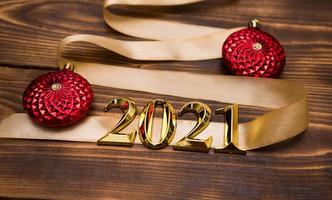 A Christmas tree made of gold ribbon with the numbers 2021 is decorated with red balloons on a dark wooden background. Flat lay. Space for text. New year, Santa hat. photo