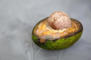 Spoiled avocado with green mold and black spots of rot and fungus on a gray background. Cut natural fruit, half with a round bone. Space for text photo