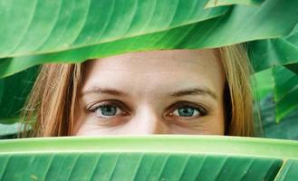 closeup of young woman eyes looking from palm trees leaves photo