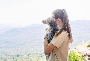 mujer joven sosteniendo un pequeño cachorro de perro yorkshire terrier caminando por las montañas foto