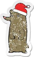 retro distressed sticker of a cartoon bear in xmas hat vector