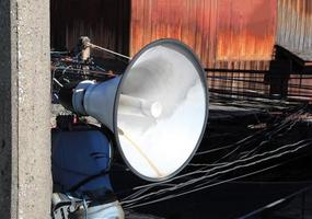 White vintage horn loudspeaker installed on the pole for boardcasting information in community with messy wires in background. photo