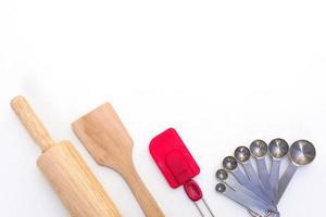 Top view kitchenware wooden rolling pin, wooden spatula, silicone spatula and steel measuring spoons on white background. photo