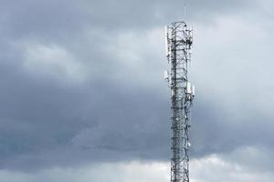 concepto de comunicación y tecnología. torre de telecomunicaciones de la estación base de telefonía celular, torre de telecomunicaciones inalámbrica del transmisor con nubes negras en el cielo o nubosidad. foto