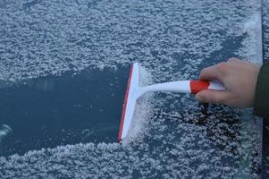 hombre raspando nieve congelada de las ventanas del auto durante la nevada foto