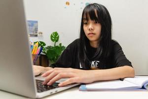 Asian teen girl use computer laptop technology internet online research information social network and education homework on table. photo