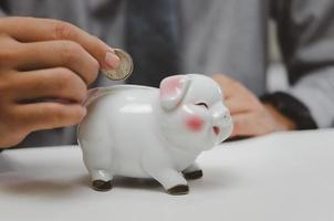 Businessman holding money coin saving finance investment income currency piggy bank on table business concept. photo