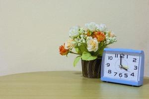Closeup alarm blue clock, 4 o'clock with flower on wall background photo