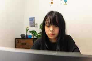 Asian teen girl use computer laptop technology internet online research information social network and education homework on table. photo