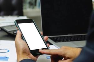 Man holding mobile smartphone mock up blank white screen and computer laptop document graph on desk.clipping pahts. photo