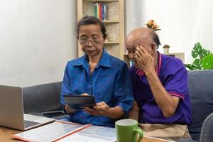Asian elderly sit and holding calculator for insurance or medical expenses and a computer on desk home. photo