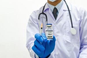 médico masculino con guantes médicos uniformes sosteniendo una botella de virus de la vacuna covid 19 sobre fondo blanco. copie el espacio. foto