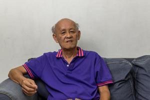 retrato de un anciano asiático sentado en el sofá de casa. foto
