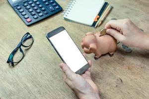 Human hand holding mobile smart phone with hand putting money in a piggy photo