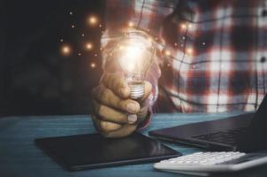 Hand holding light bulbs and book opening on wooden table.Creative thinking ideas for work on desk.searching for new ideas,Knowledge,successful, wisdom.Photo concept of knowledge and education. photo