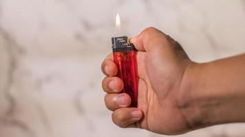 hand of man lighting cigarette lighter against bright background photo