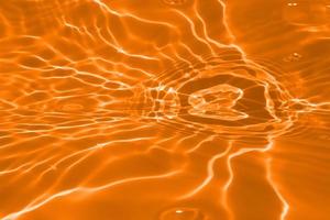 Defocus blurred transparent orange colored clear calm water surface texture with splashes and bubble. Trendy abstract nature background. Water wave in sunlight with copy space. Orange water drop color photo