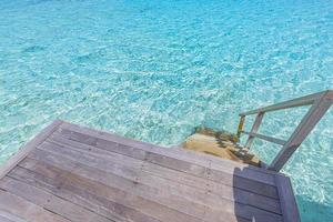 Wooden platform with steps to azure sea water in Maldives islands. Stairway goes down to the ocean lagoon from overwater villa, summer vacation, tropical holiday template. Luxury background concept