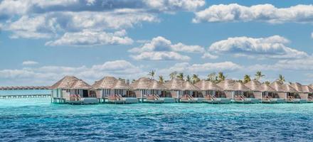 vista aérea de la isla de maldivas, resort de lujosas villas acuáticas y muelle de madera. hermoso cielo y fondo de la playa de la laguna oceánica. concepto de vacaciones y viajes de vacaciones de verano. paraíso aéreo paisaje pano