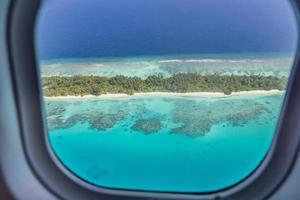Airplane window with beautiful Maldives island view. Luxury summer holiday travel tourism background, view from airplane window. Atolls and islands with amazing tropical sea photo