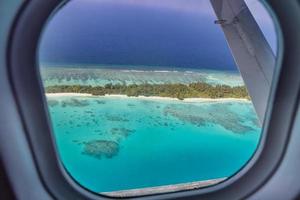 Airplane window with beautiful Maldives island view. Luxury summer holiday travel tourism background, view from airplane window. Atolls and islands with amazing tropical sea photo