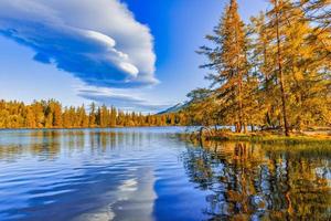 Beautiful golden colored trees with autumn lake landscape. Tranquil autumn sunset. Calm morning view of Strbske pleso lake. Amazing nature outdoor of High Tatra National Park, Slovakia, Europe photo