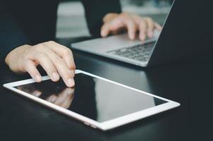 hombre de negocios con una tableta táctil y una computadora portátil busca información con tecnología de Internet trabajando en el escritorio. foto