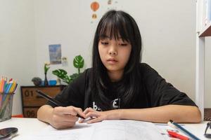 Asian student girl is writing homework and reading book at desk photo