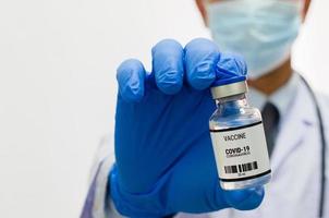 médico masculino con guantes médicos uniformes sosteniendo una botella de virus de la vacuna covid 19 sobre fondo blanco. copie el espacio.