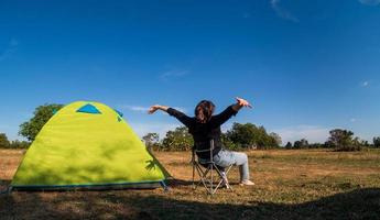 Asian female tourists are sitting happy free with green tent for traveler sits on  wide field, overlooking evening time Of Private area Thailand for camping getaway During long holiday for travel. photo