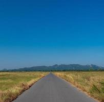 largo camino que recorre varios pueblos en las zonas rurales de tailandia pasando por prados forestales y montañas en un día despejado cielo azul nube blanca en verano conducción adecuada foto