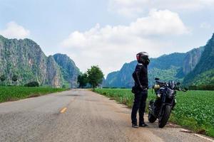 vista frontal de viajar solo camino montaña cielo, casco, vistiendo ropa protectora negra tome una motocicleta de aventura negra kawasaki er6n journry a varios lugares. foto